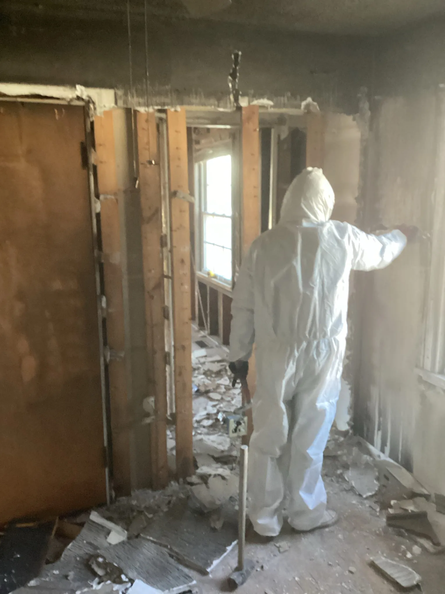 Technician in a white protective suit assessing a fire damaged room stripped to the studs