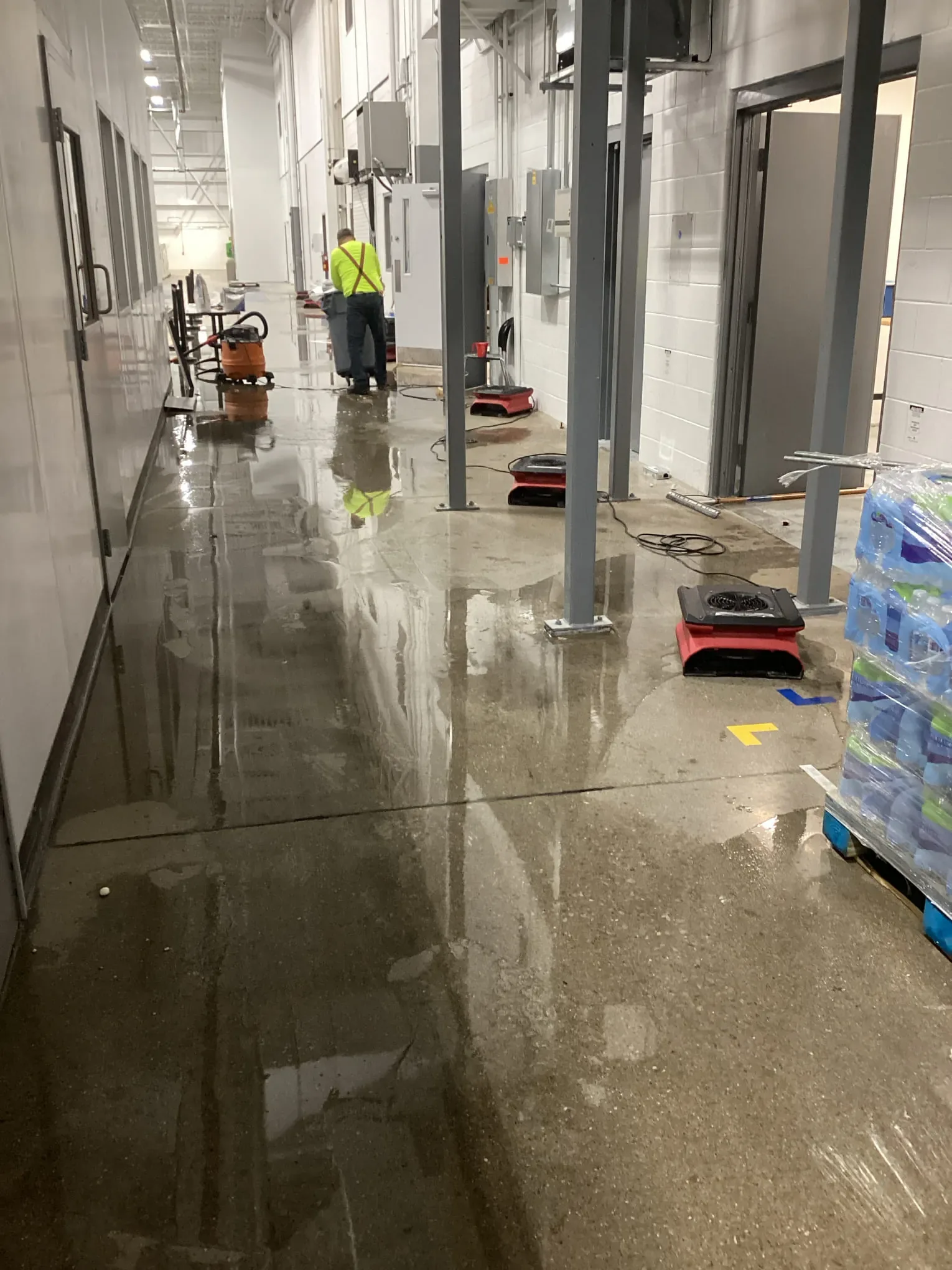 Technician working along a flooded commercial hallway with extraction and drying equipment