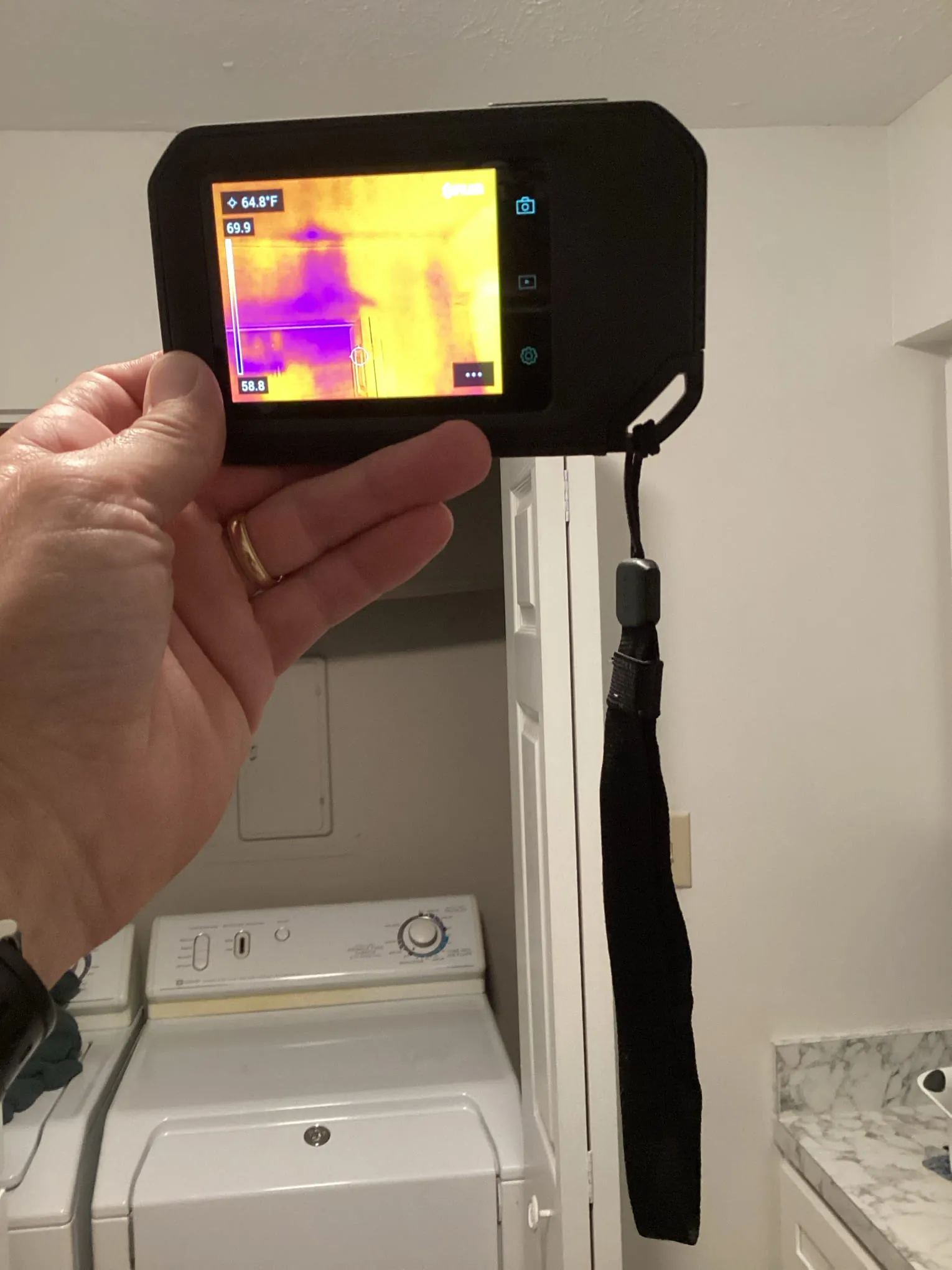 Technician holding a thermal imaging camera showing moisture readings inside a Louisville laundry room